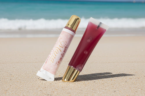 Lip gloss with gold cap and pink packaging on a textured surface